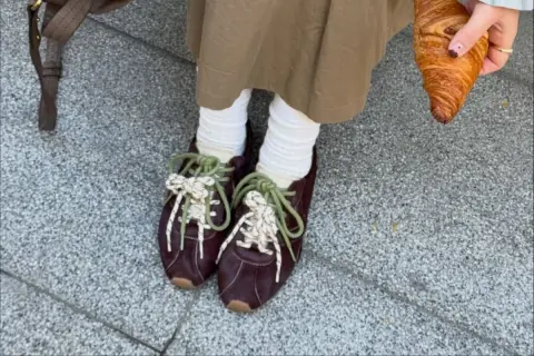 Modne sneakersy 2026 w bordowym kolorze, z zielonymi i białymi sznurówkami, idealne na spacer z croissantem.