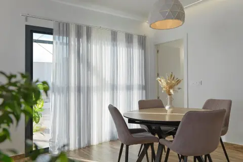 Comedor moderno con mesa y sillas, y diferentes tipos de cortinas que filtran la luz.