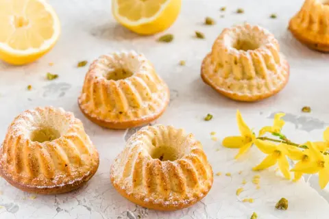 Szybkie babeczki wielkanocne, oprószone cukrem pudrem, z cytryną i pistacjami w tle.