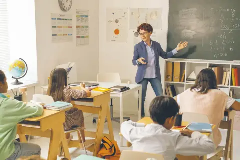 Nauczycielka tłumaczy zadanie, dzieci słuchają. Ile godzin tygodniowo pracuje nauczyciel przedszkola? To pytanie pozostaje bez odpowiedzi, ale lekcja trwa.