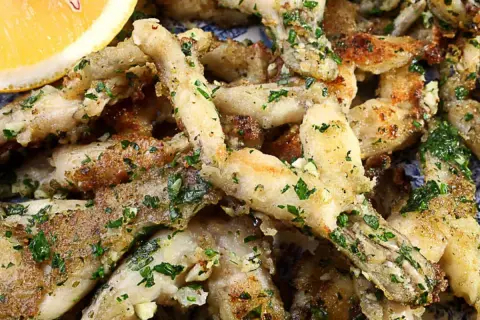 Un plat de cuisse de grenouille frite, garni de persil frais et d'ail, servi avec un quartier de citron.