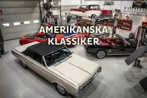 En samling amerikanska klassiker, inklusive 70 tals bilar, i ett garage. En beige cabriolet står i förgrunden.