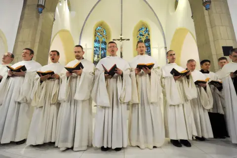 Mönche in weißen Roben singen gregorianik musik aus Büchern in einer Kirche.