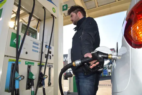 Mężczyzna tankuje benzynę do Skody Fabii 1.2. Dłoń trzyma pistolet paliwowy przy samochodzie.