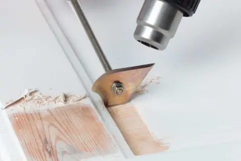 Heißluftföhn und Schaber entfernen alten Lack von Holz.