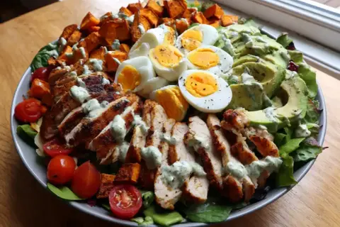 En stor, matig sallad med grillad kyckling, ägg, sötpotatis, avokado och körsbärstomater, toppad med en krämig dressing.