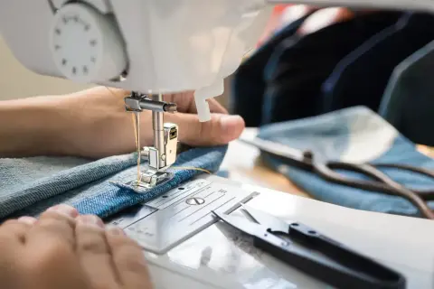 Ręce szyjące na maszynie dżinsową spódnicę. Instrukcja, jak wszyć gumkę do spódnicy, krok po kroku.
