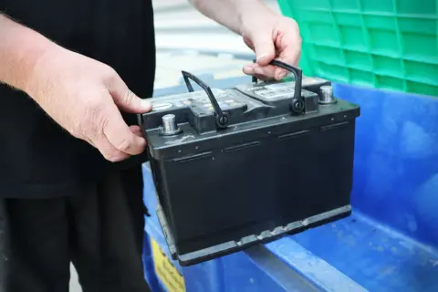 Händer placerar ett bilbatteri i en blå behållare. Kanske för återvinning eller för att byta ut dubbla batterier i bilen.