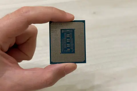 Un dedo sostiene un procesador o CPU, mostrando su parte inferior con pines dorados y un diseño rectangular en el centro.