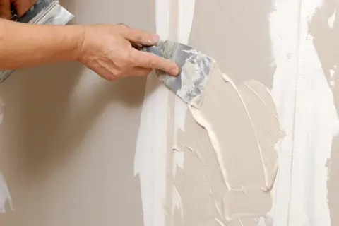 Mano stende stucco su una giuntura di cartongesso, ricordando che il cartongesso ha un verso.