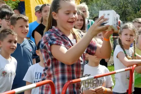 Dziewczynka trzyma pudełko na festynie rodzinnym, otoczona innymi dziećmi.