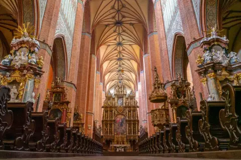 Wnętrze katedry z ceglanymi filarami, bogato zdobionym ołtarzem i rzędami drewnianych ławek. Wspaniały łęg gotyckiej architektury.