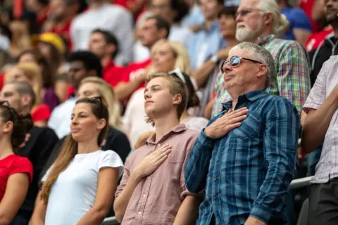 Ludzie na trybunach, z rękami na sercach, słuchają hymnu.