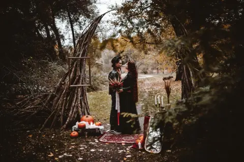 Para w czarnych strojach pod łukiem z gałęzi, dynie i świece.