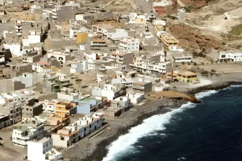 Vista aérea de un pueblo costero en las maretas Tenerife, con casas blancas y de colores apiladas en una ladera rocosa junto al mar azul.