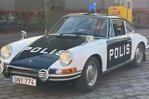 En klassisk Porsche polisbil med blåljus på taket. Bilen är vit med svarta detaljer och texten "POLIS" på motorhuven och dörren.
