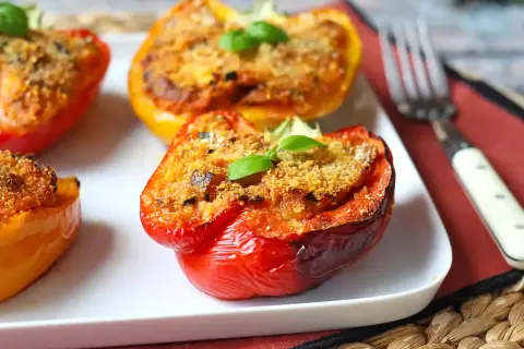 Poivrons farcis colorés, dorés et appétissants, garnis d'une chapelure croustillante et d'une feuille de basilic frais.