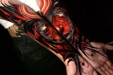 Arm-Tattoos mit roten Tattoos, die ein dämonisches Gesicht mit roten Augen und scharfen Zähnen darstellen.