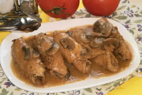 Pyszne gołąbki z pieczarkami w sosie, podane na białym talerzu. Obok stoją pomidory i przyprawniki.