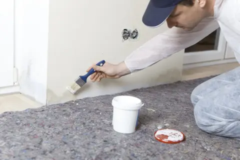 Maler streicht mit Pinsel über Wasserflecken an der Wand, um sie zu überdecken.