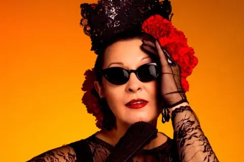 Jarcha, con su estilo inconfundible, evoca un martirio flamenco con encaje negro, gafas oscuras y flores rojas sobre fondo naranja.