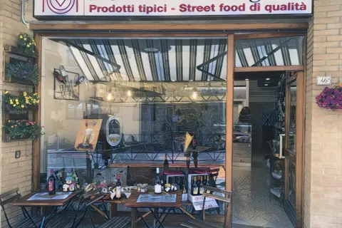 Delizie Marchigiane: prodotti tipici e street food di qualità ad Ancona. Tavolini all'esterno invitano a gustare le specialità locali.