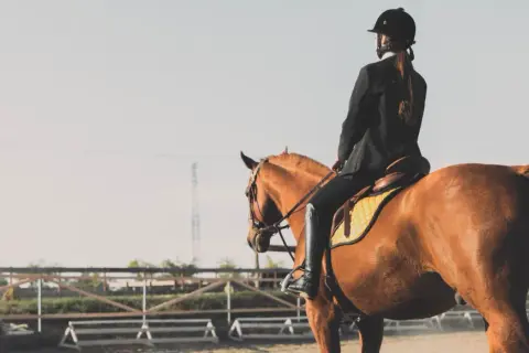Une cavalière en tenue d'équitation, le périnée bien soutenu, monte un cheval brun dans une carrière.
