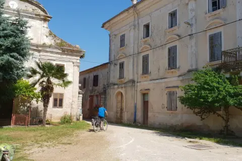Ciclistas exploran un pueblo antiguo en Croacia, con edificios de piedra y vegetación exuberante.