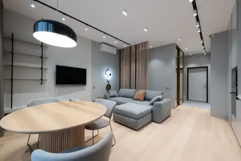 Nowoczesny salon z szarą kanapą i drewnianym stołem. Ściany w odcieniu cool white, jasna podłoga.