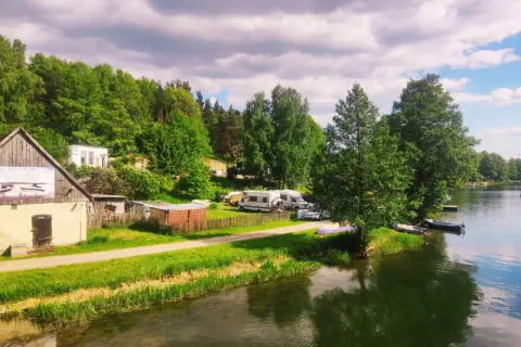 Malowniczy widok na jezioro i lasy, gdzie leżą Bory Tucholskie. Kemping z kamperami i łodziami przy brzegu.