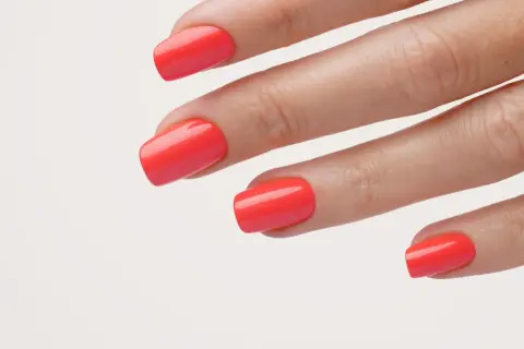 Main d'une femme avec un vernis corail vif, parfait pour un ongle vacances.