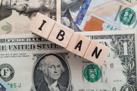 Drewniane klocki z napisem IBAN leżą na banknotach dolarowych. Dowiedz się, jak sprawdzić IBAN.