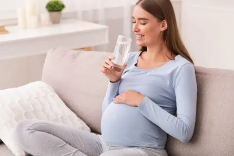 Kobieta w ciąży pije wodę, dbając o swoje zdrowie i prawidłowe cukrzyca ciążowa normy.