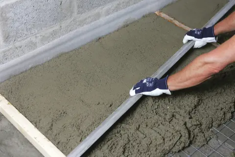 Ręce w rękawiczkach wygładzają świeży styrobeton za pomocą łaty.