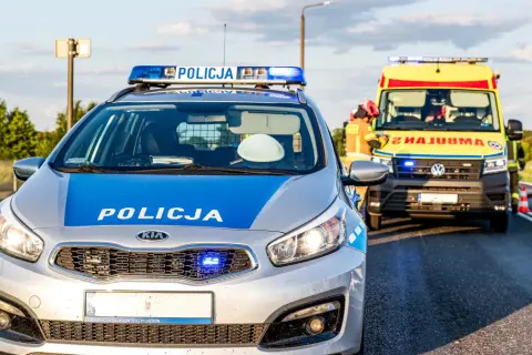 Radiowóz policyjny i karetka na poboczu drogi w Emilianowie. Służby zabezpieczają miejsce zdarzenia.