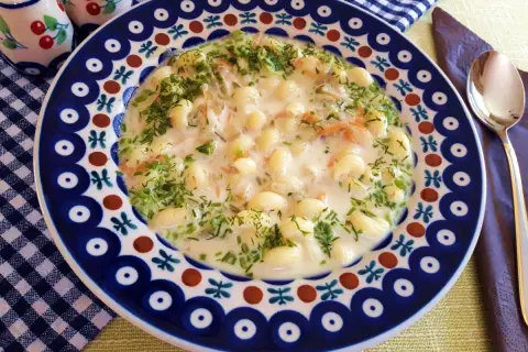 Pyszna zupa na wywarze z golonki z makaronem i koperkiem, podana w ozdobnym talerzu.