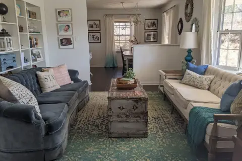 A living room with two sofas, a vintage trunk coffee table, and a patterned rug. This space shows how to brighten a dark room with light-colored furniture and ample natural light.