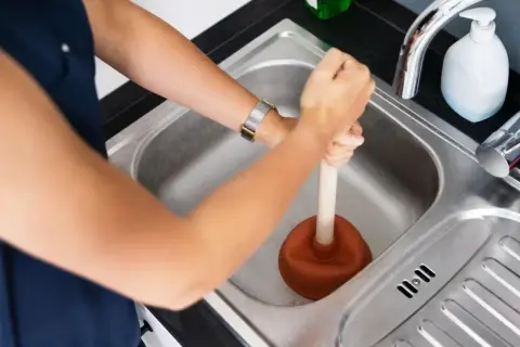 Une personne utilise une ventouse pour déboucher la canalisation d'eau chaude de l'évier.