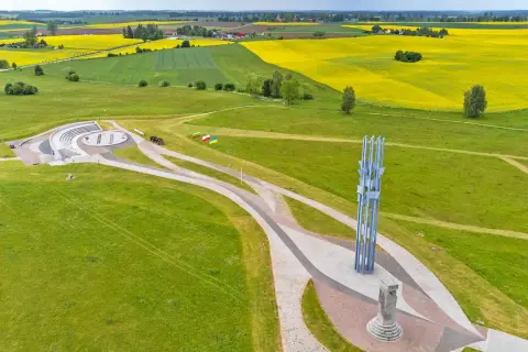 Pomnik Grunwaldzki i amfiteatr na tle pól rzepaku. Trasa turystyczna prowadzi przez zielone wzgórza.