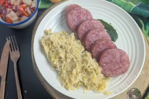 Piatto con fette di cotechino fresco e crauti, accompagnato da un'insalata di verdure e pane. Perfetto per la cottura.
