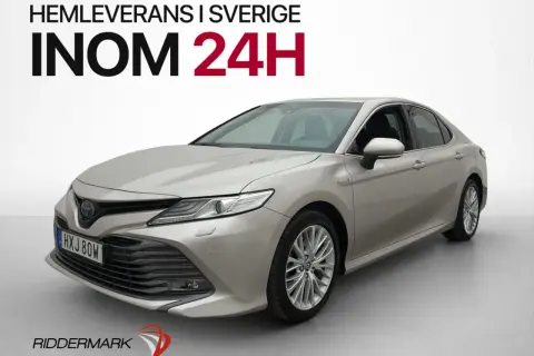 En silverfärgad, begagnad Toyota Camry hybrid visas framifrån. Hemleverans inom 24 timmar i Sverige.