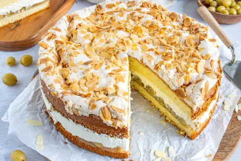 Eine köstliche Stachelbeer Baiser Torte, mit Baiserhaube und Mandelblättchen, daneben ein Stück Torte mit saftiger Füllung.