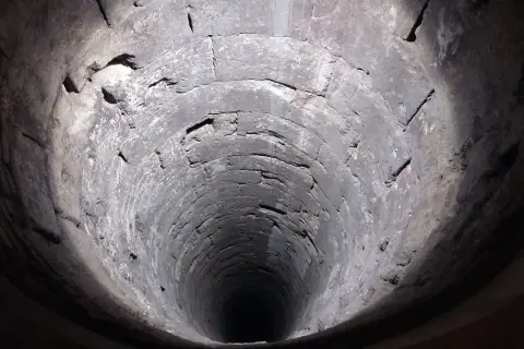 Blick in einen alten, steinernen Brunnen. Die Wände sind rau und uneben, was auf die Notwendigkeit hinweist, den Brunnen abzudichten.