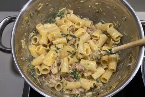 Rigatoni mit cremiger Sauce, Fenchel und Salsiccia. Ein Holzlöffel rührt die köstliche Pasta in einem Topf.