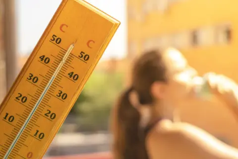 En termometer visar över 30 grader. En person dricker ur ett glas. Frågan är hur varmt får det vara på jobbet?