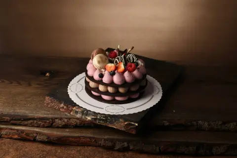 En vacker tårta med macarons, bär och chokladdekorationer, serverad på ett rustikt träfat.