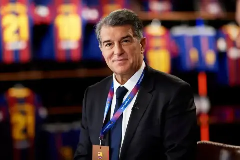 Prezes FC Barcelona, Joan Laporta, w garniturze, z identyfikatorem klubu na szyi, na tle klubowych koszulek.