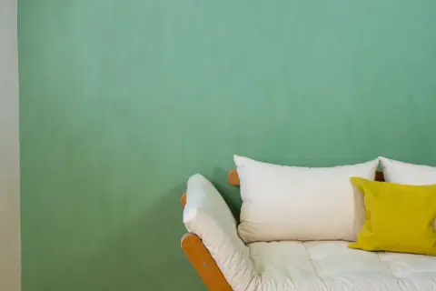 Ein Sofa mit weißen und gelben Kissen vor einer mintgrünen Wand. Die Frage "wieviel Wandfarbe pro qm" wird hier nicht beantwortet.
