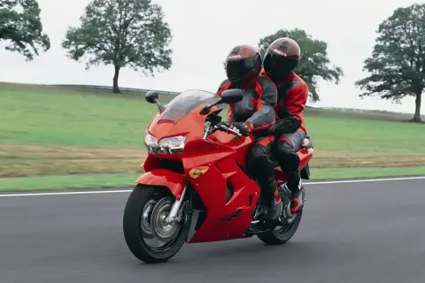 Dwie osoby w czerwonych kombinezonach jadą na czerwonym motocyklu Honda VFR 800.