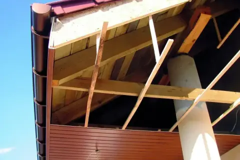 Widok od spodu na konstrukcję dachu z widoczną podprzybitką, rynną i kominem.